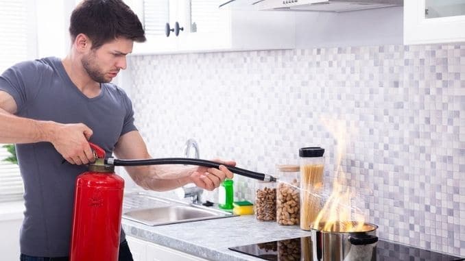 Man-Using-Fire-Extinguisher-To-Stop-Fire-On-Burning-Cooking-Pot-In-The-Kitchen